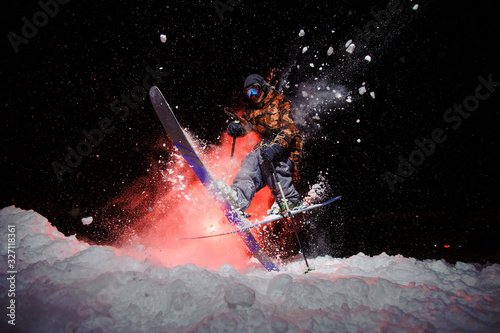 Male skier dressed in a grey orange sportswear jumping under the snow with sticks