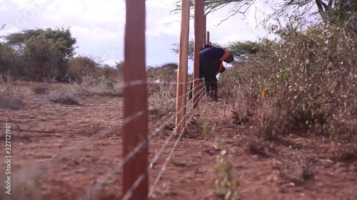 Men construct a long barbed wired fence, security Africa, Kenya, shallow DOF
