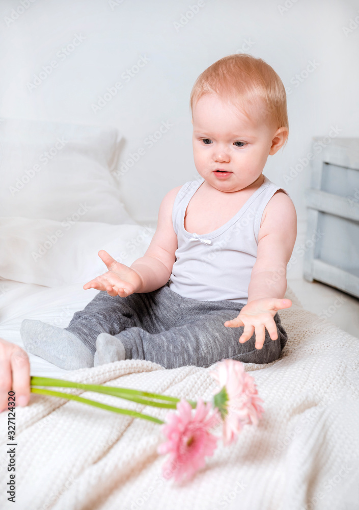 baby, little white blonde girl sitting on a bed with pink gerbera flowers baby, little white blonde girl sitting on a bed with pink gerbera flowers