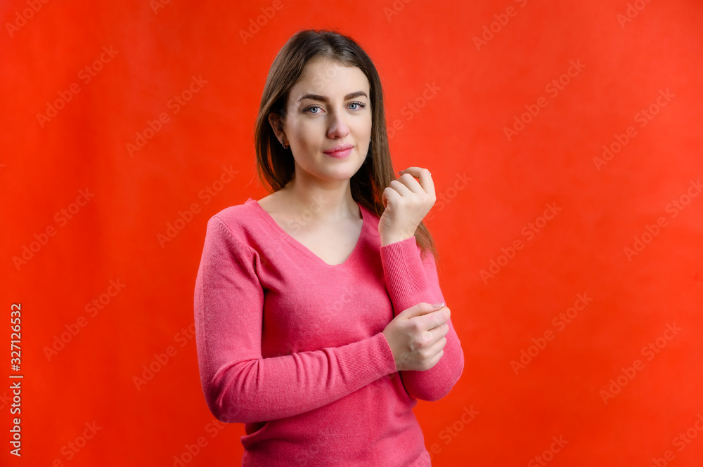 Photo on a red background of a serious pretty Caucasian woman in a pink sweater