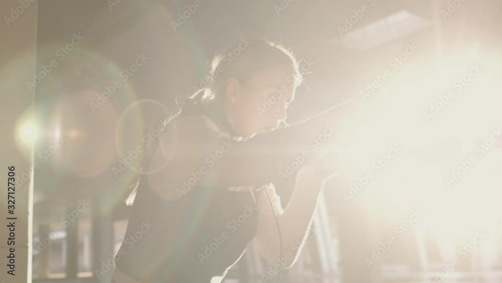 Athletic female doing shadow boxing workout in urban area. Shot in slow motion with dusty particles shimmering in the sunlight.