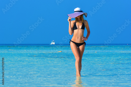 Fit girl on a tropical beach with hat. Sexy black bikini body woman on paradise tropical beach. Beautiful fit body girl on travel vacation. Banner crop for copy space. Fashion photo of sexy hot girl.
