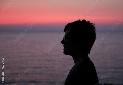 black profile of boy with glasses and the sea at sunset