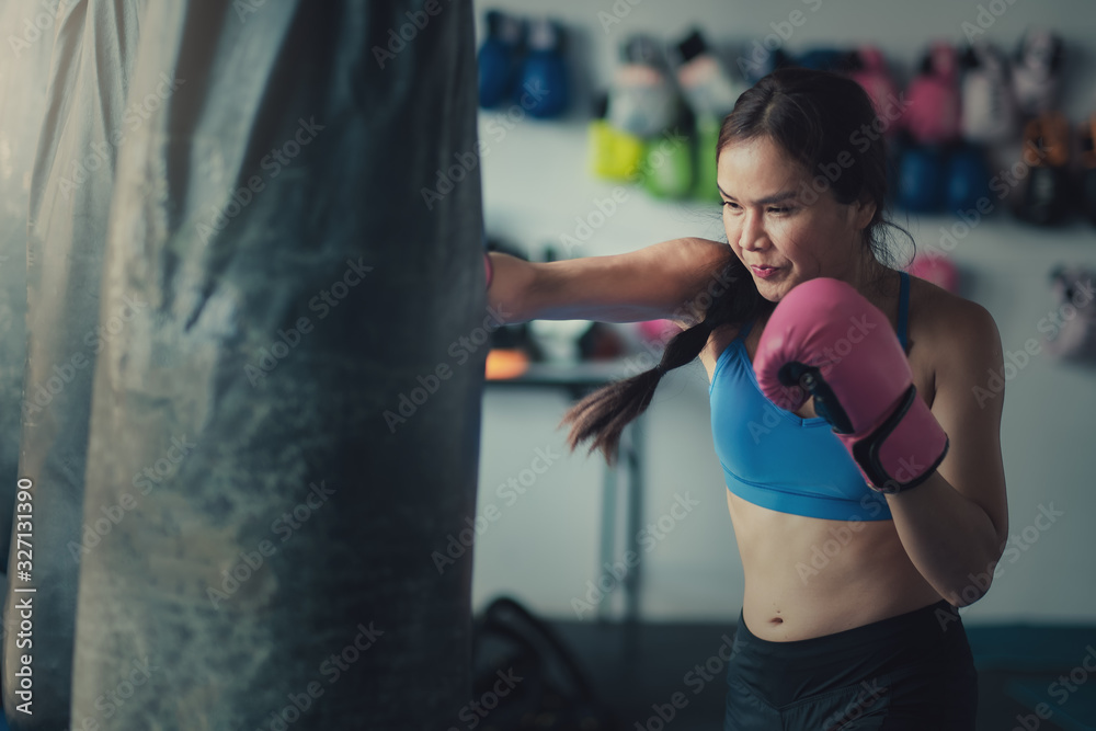 Female boxer hitting a punching bag with boxing gloves at gym. Women training hard