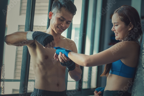 Personal trainer helping young female boxer wrap her hand with strap in gym