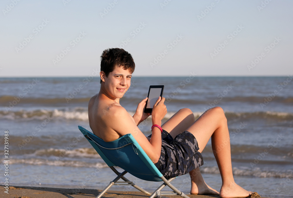 young boy reads ebook on the beach