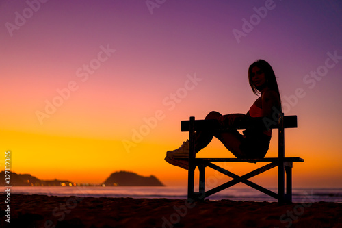 Lifestyle, beautiful silhouette of a brunette in a chair on the beach on a sunset looking at the sea