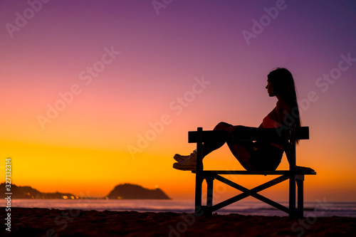 Lifestyle, beautiful silhouette of a brunette in a chair on the beach at a sunset