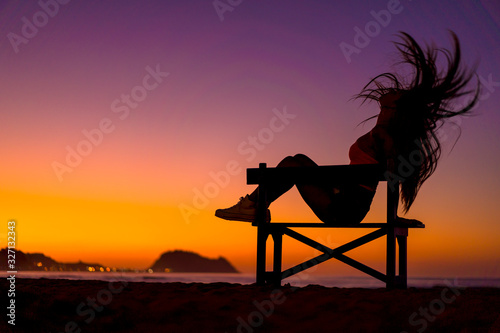 Lifestyle  silhouette of a brunette in a chair on the beach at night on a sunset