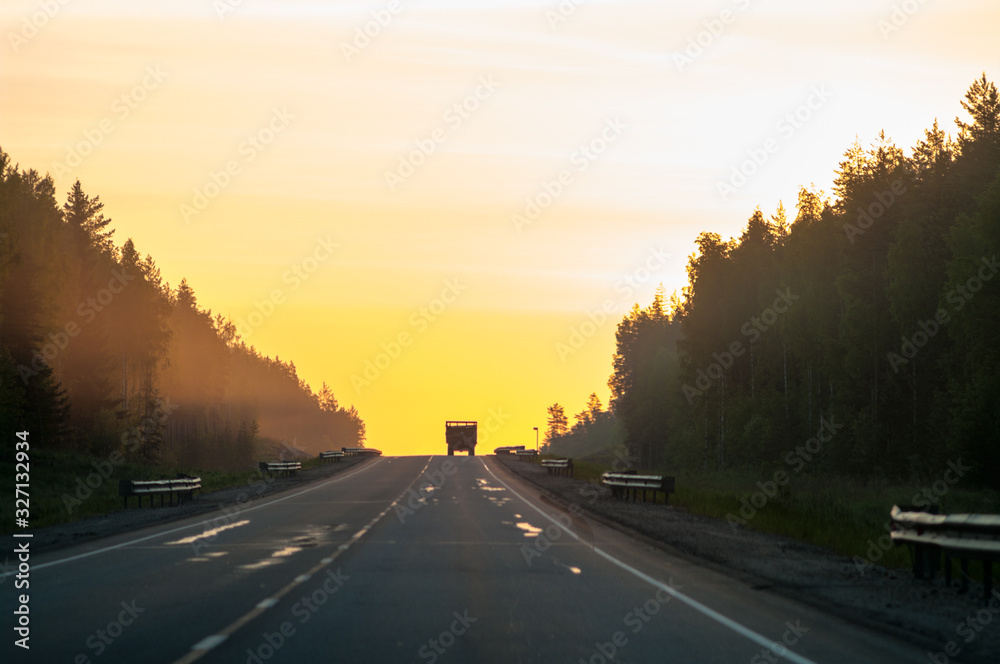 Driving away freight truck silhouette is on horizon, lorry is on distance on highway in sunrise light