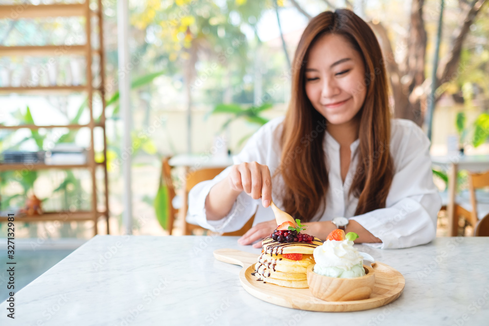 A beautiful asian woman eating a mixed berries pancakes with ice cream and whipped cream by wooden spoon A beautiful asian woman eating a mixed berries pancakes with ice cream and whipped cream by wooden spoon