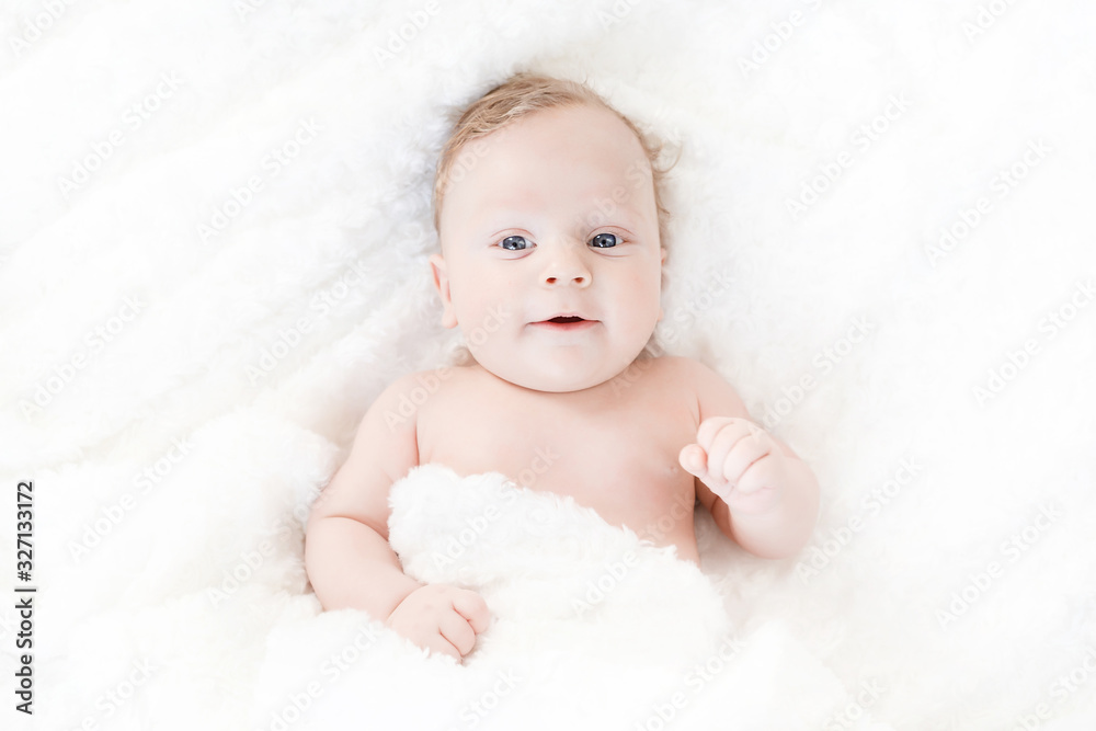 four-month-old white boy with blue eyes lies on a white blanket and take cover with him four-month-old white boy with blue eyes lies on a white blanket and take cover with him