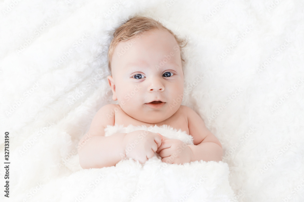 four-month-old white boy with blue eyes lies on a white blanket and take cover with him four-month-old white boy with blue eyes lies on a white blanket and take cover with him