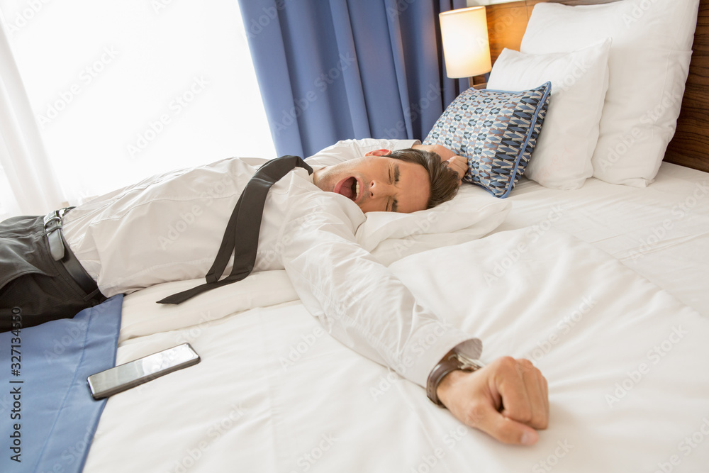 Tired businessman in suit stretching on a hotel bed Tired businessman in suit stretching on a hotel bed