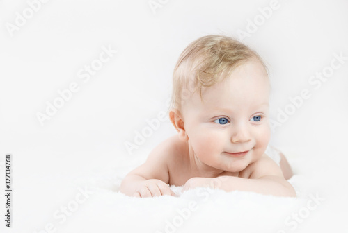 five-month-old blond boy with blue eyes lies on his stomach on a white background