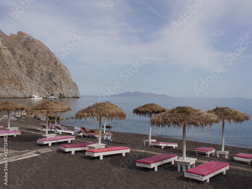 Parasols and empty sun loungers  on the black sand of Perissa Beach. 