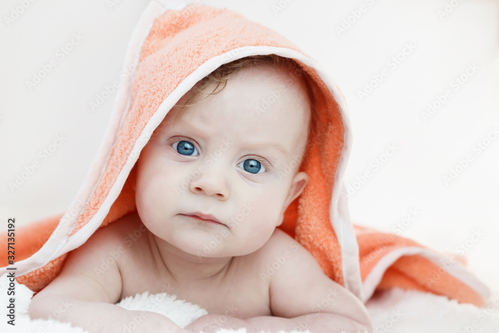 five-month-old blond boy in an orange towel with blue eyes lies on his stomach on a white background five-month-old blond boy in an orange towel with blue eyes lies on his stomach on a white background