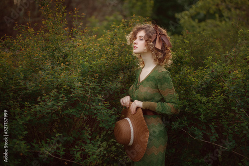 portrait of a young beautiful girl with curly hair in a hat on a green background with natural light