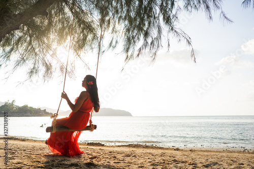girl in a red dress on a swing among tropical palm trees in Thailand at sunset