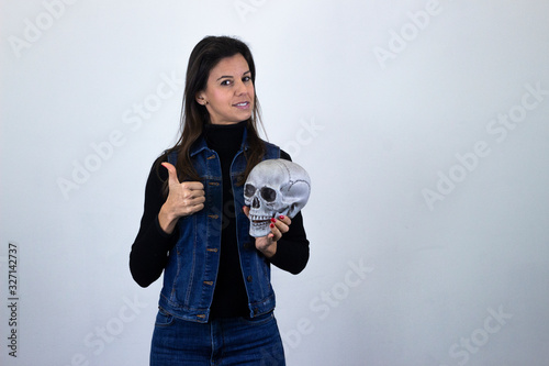 pretty  middle age woman model with skull showing thumbs up gesture, isolated on gray background studio shotblack sweater, denim jacket, jeans. Place for your text in copy space. photo