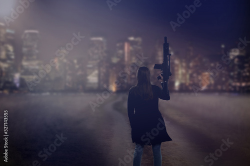 Young girl with machine gun stands on the road to the city and empty space for text