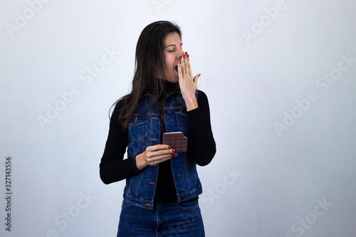 Bosteza durmiendose calm and cute bussiness womanchocolatecovers mouth with hand, yawns sleeping with closed eyes, isolated on gray background studio shot, black sweater, denim jacket, jeans, dark air