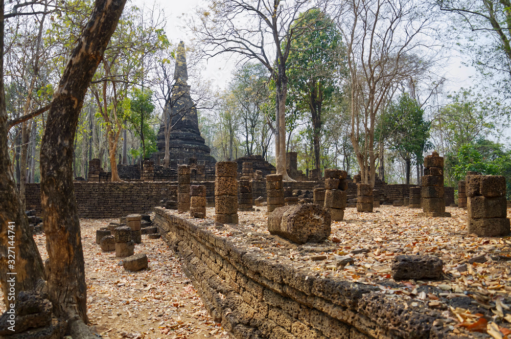 Ruins of Ancient Thai Temple (Wat Chedi Kao Yod). Trees grow between ancient stones. Si Satchanalai historical park, Northern Thailand.