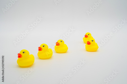 Five mini yellow rubber ducks in a row. One duck out of line. Ge