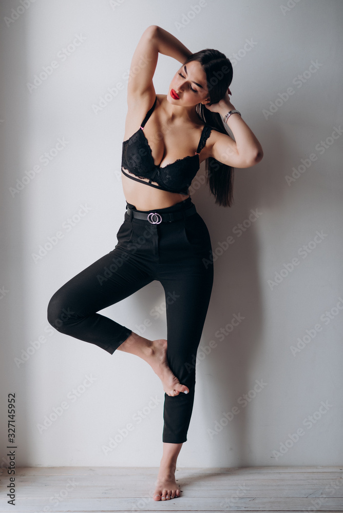 a young girl with dark hair, brown eyes and bright red lips poses in a Studio in black underwear and black trousers