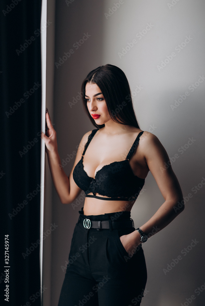 a young girl with dark hair, brown eyes and bright red lips poses in a Studio in black underwear and black trousers a young girl with dark hair, brown eyes and bright red lips poses in a Studio in black underwear and black trousers