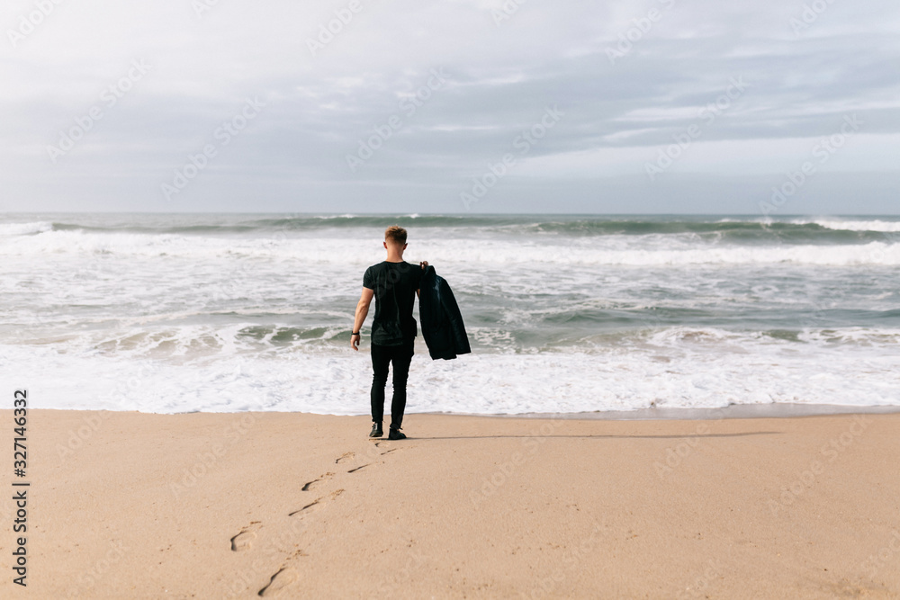 Full-lenght outside portrait of man in casual clothes walking by the ocean, blue sky and waves Full-lenght outside portrait of man in casual clothes walking by the ocean, blue sky and waves
