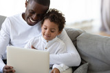 Loving African American father teaching little son to use laptop