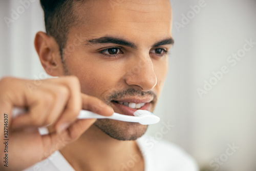 Smiling young man is using toothbrush at home