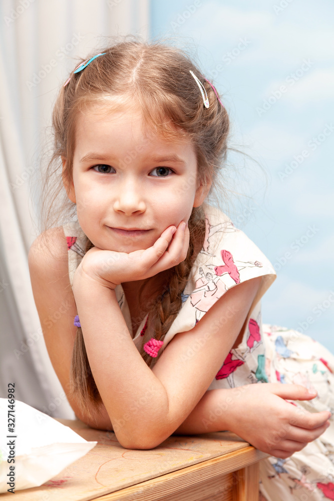 Little young happy smiling school girl smiling, leaning on a table with hand under her chin portrait. Smug smirk expression. Small beautiful healthy causasian kid with hairpins frontal shot, happiness Little young happy smiling school girl smiling, leaning on a table with hand under her chin portrait. Smug smirk expression. Small beautiful healthy causasian kid with hairpins frontal shot, happiness