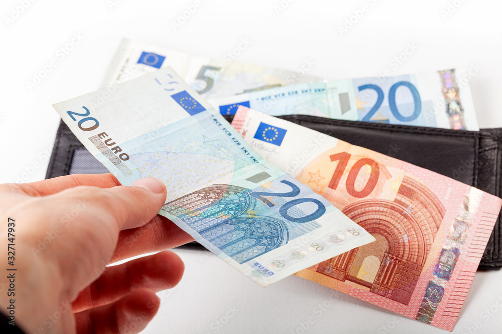 Hand adding money to the heap of european euro banknotes, small bills laying on the black wallet Saving money, cashback, contribution, efficient successful financial management symbol abstract concept