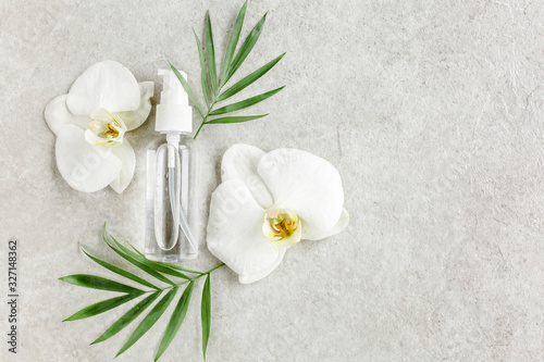 Bottle with hyaluronic acid / essential oil, tropic palm leaves on gray marble background. Concept of modern beauty. Natural / Organic cosmetics products. Flat lay, top view.