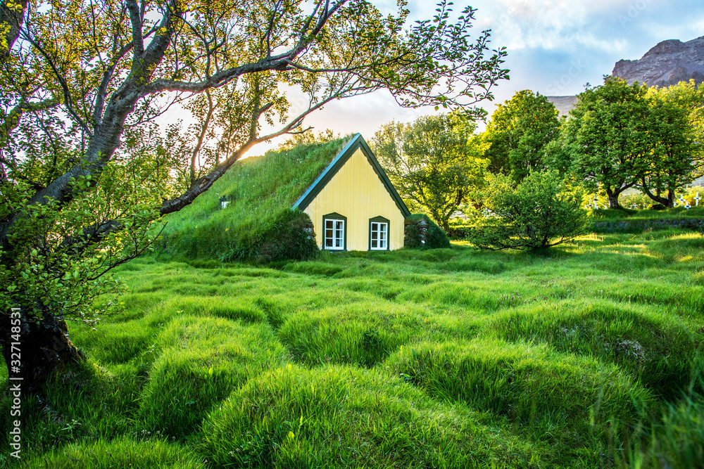 Charming mystical scene with turf roof church with windows and cemetery with small graves in Hof, Skaftafell, Vatnajokull National Park at sunset. Exotic countries.