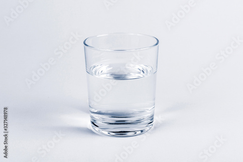 Photos One simple half full half empty glass of fresh crystal clear clean drinking water, solo object isolated on light blue background