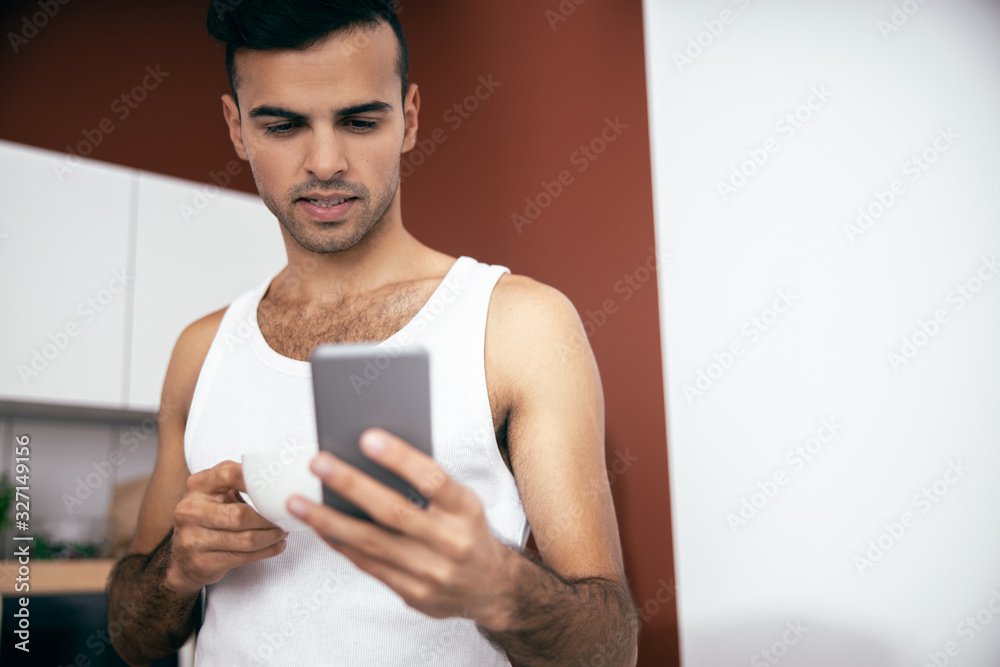 Handsome guy looking at mobile phone screen at the kitchen Handsome guy looking at mobile phone screen at the kitchen