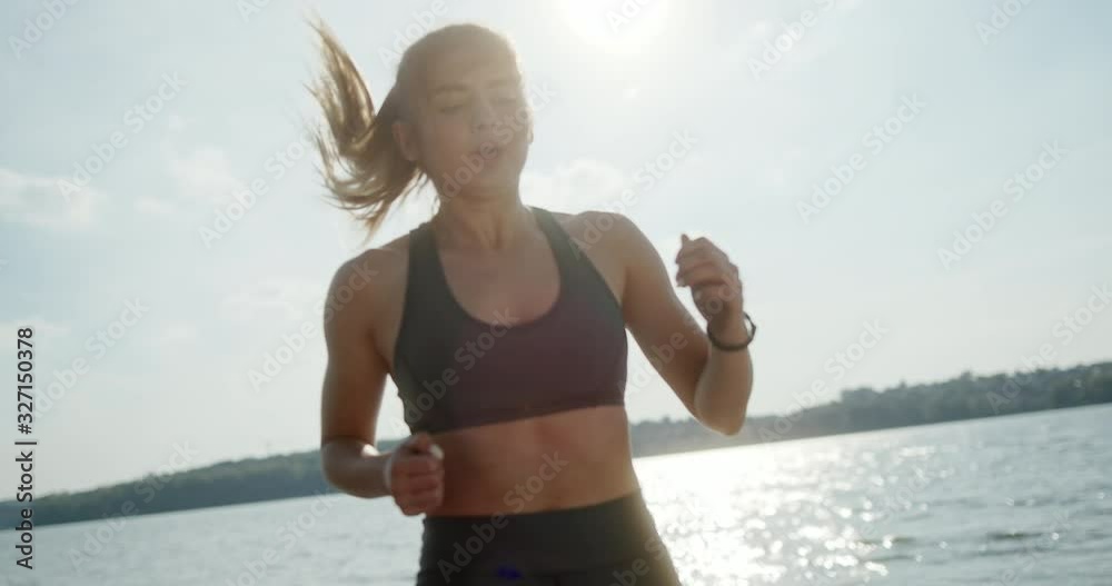 Muscular fit young woman jogging on the spot on a wooden deck overlooking water for a healthy cardiovascular workout to burn calories in a fitness and active lifestyle concept.