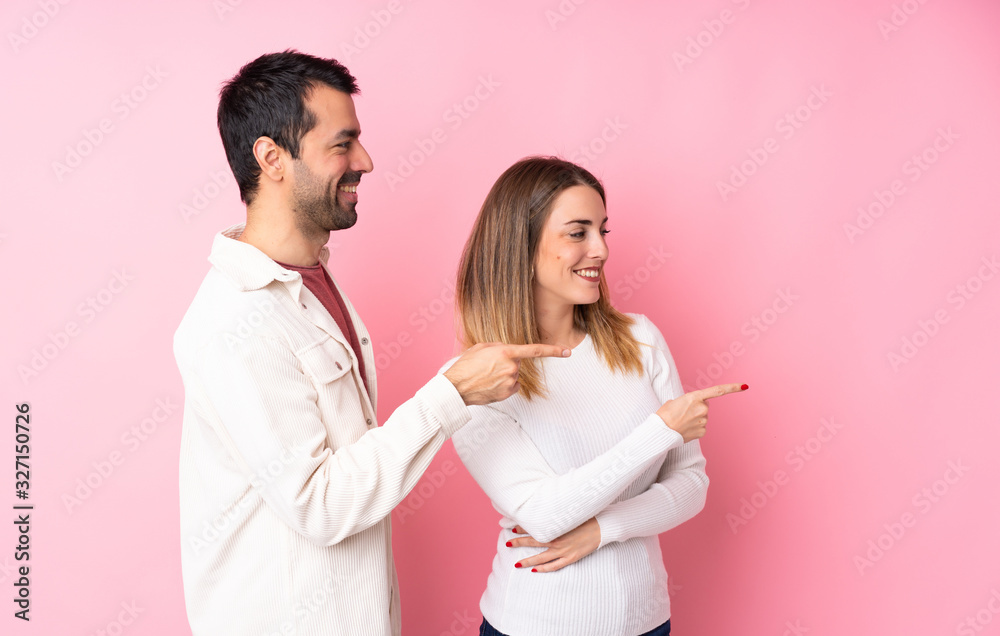 Couple in Valentine Day over isolated pink background pointing finger to the side in lateral position Couple in Valentine Day over isolated pink background pointing finger to the side in lateral position