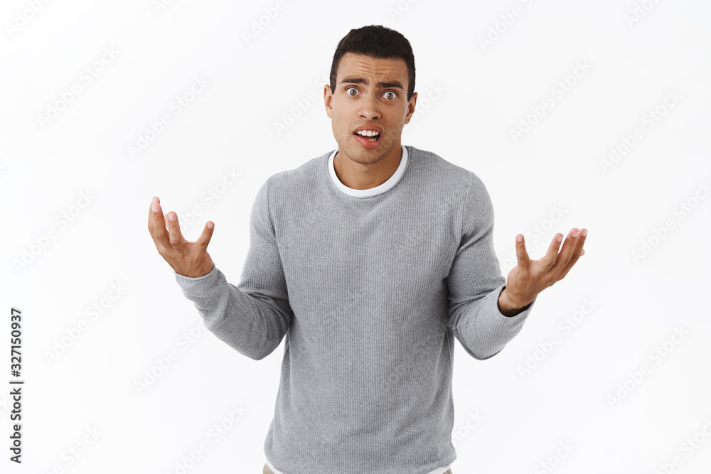 Anxious and nervous, panicking young hispanic man dont know how solve problem, shaking hands useless and alarmed, look concerned camera, standing intense and pressured over white background