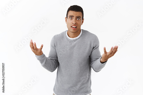 Anxious and nervous, panicking young hispanic man dont know how solve problem, shaking hands useless and alarmed, look concerned camera, standing intense and pressured over white background