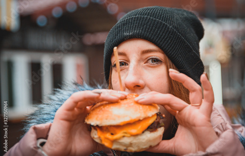 Street food. young woman holding juicy burger and eating oudoor winter