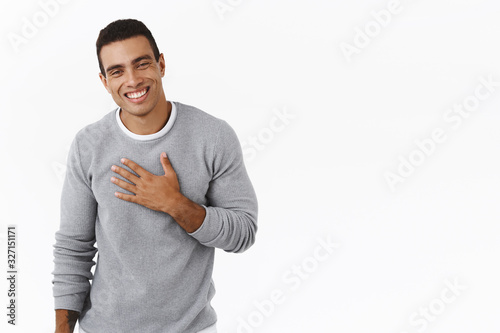 Happy and pleased, flattered hispanic man thanking for praises, holding hand on chest and smiling grateful, saying my pleasure, express gratitude and delighted, white background