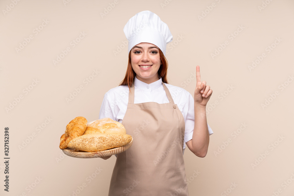 Redhead teenager girl in chef uniform. Female baker holding a table with several breads pointing up a great idea Redhead teenager girl in chef uniform. Female baker holding a table with several breads pointing up a great idea