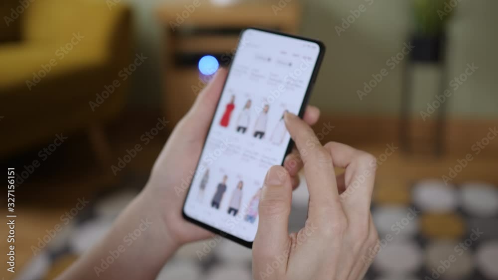 Woman Looks at Goods in Online Store Clothing. Buy Fashion Clothes Directly on Smartphone. Woman at Home Lying on Couch in Living Room Using Smartphone Buys in Internet Shop.