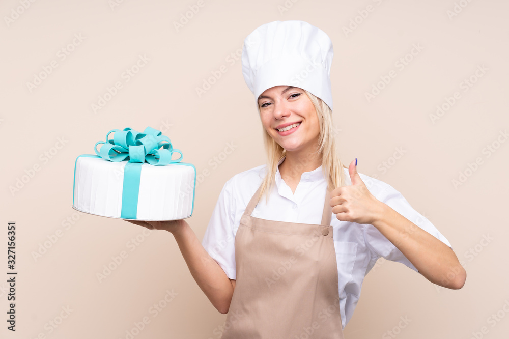 Young Russian woman with a big cake over isolated background with thumbs up because something good has happened Young Russian woman with a big cake over isolated background with thumbs up because something good has happened