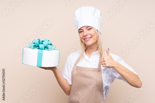 Young Russian woman with a big cake over isolated background with thumbs up because something good has happened