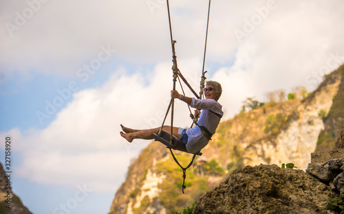 mature attractive and happy woman on with grey hair enjoying amazing rock cliff view from swing feeling young and free swinging carefree having beautiful retirement